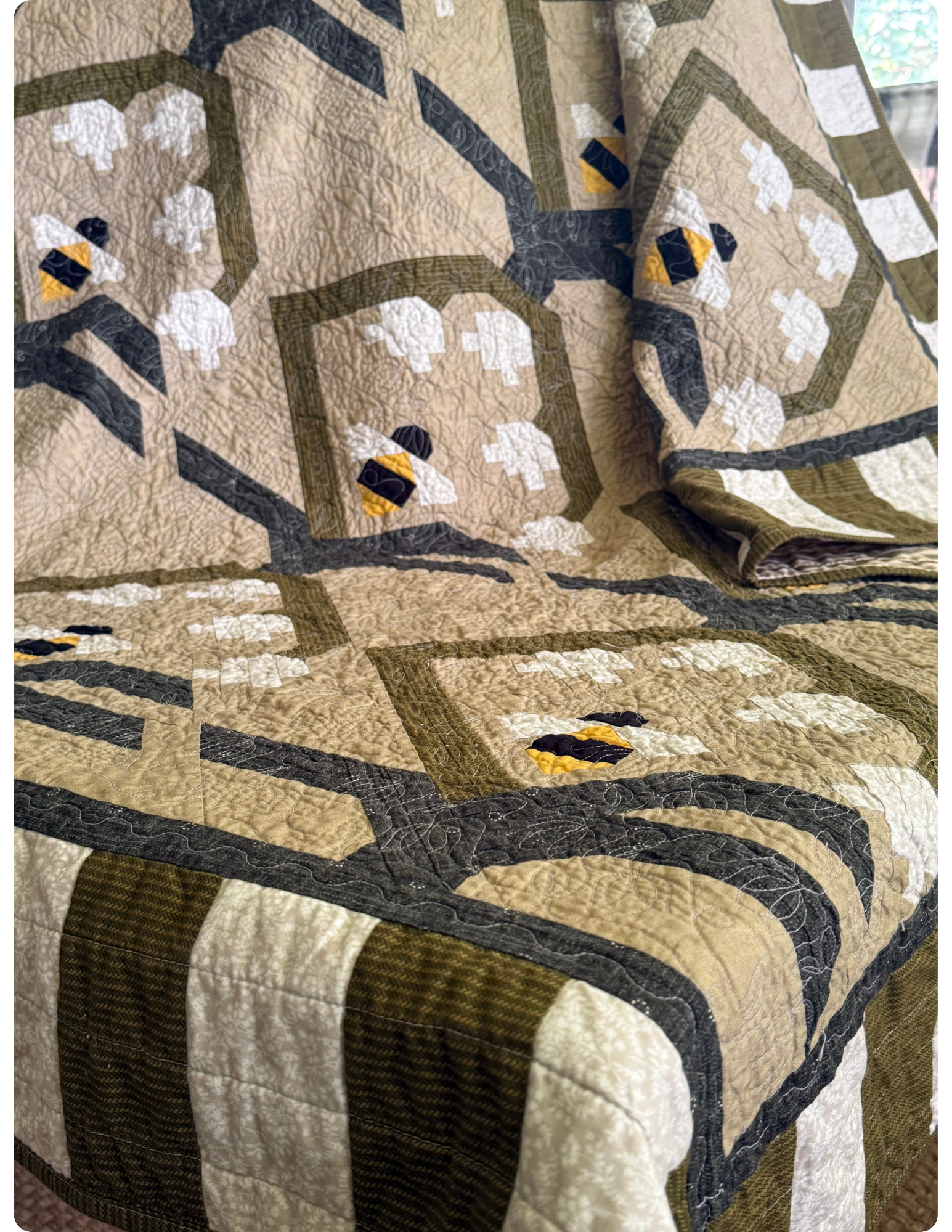 Angled view of quilt with green and white stripe border. 3x4 flower and bee quilt block in the center.