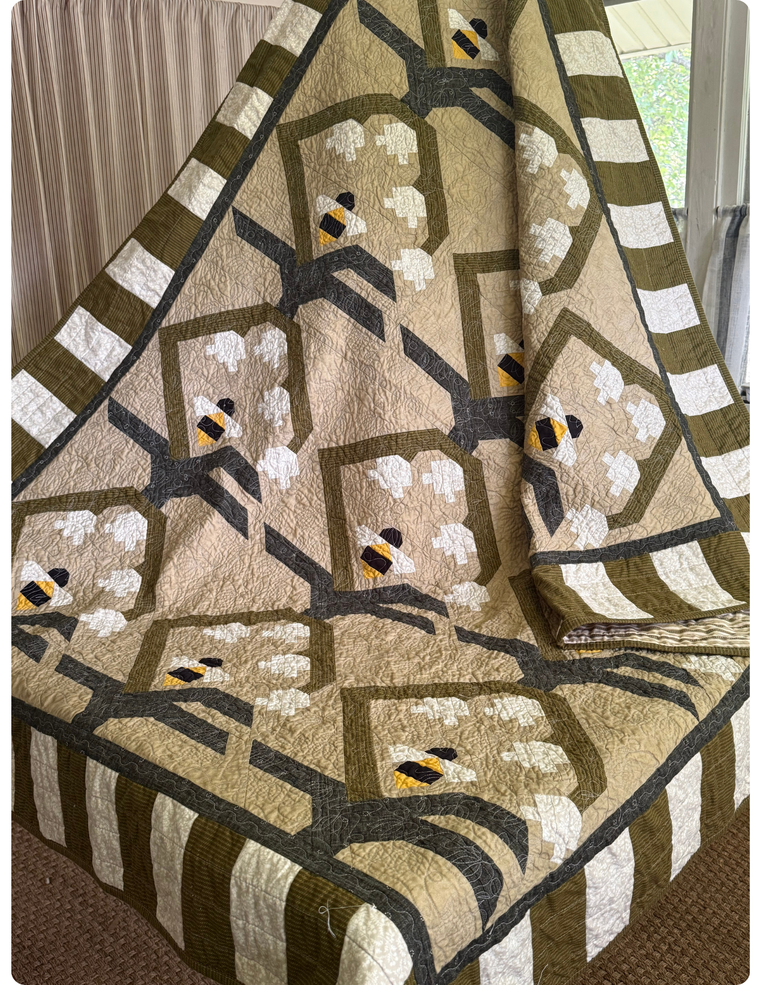Angled view of quilt with green and white stripe border. 3x4 flower and bee quilt block in the center.